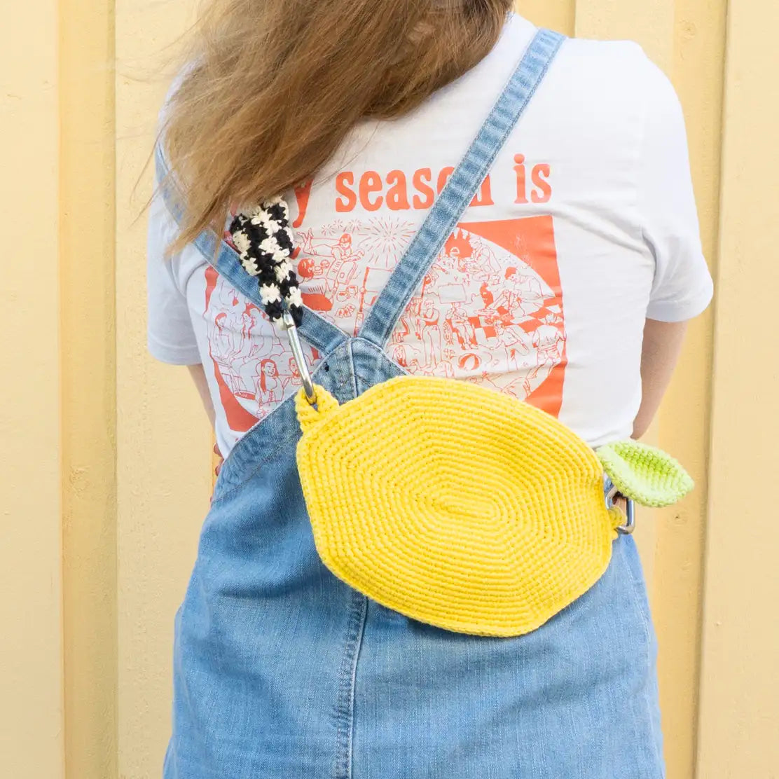 A human wearing a yellow crochet lemon cross-body bag with zipper and a black and white striped bag strap