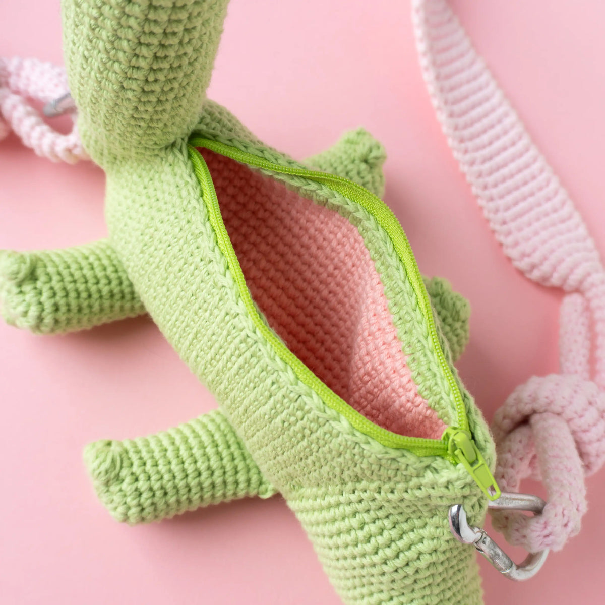 Crocheted brachiosaurus dinosaur bag on a pink background.