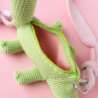 Crocheted brachiosaurus dinosaur bag on a pink background.