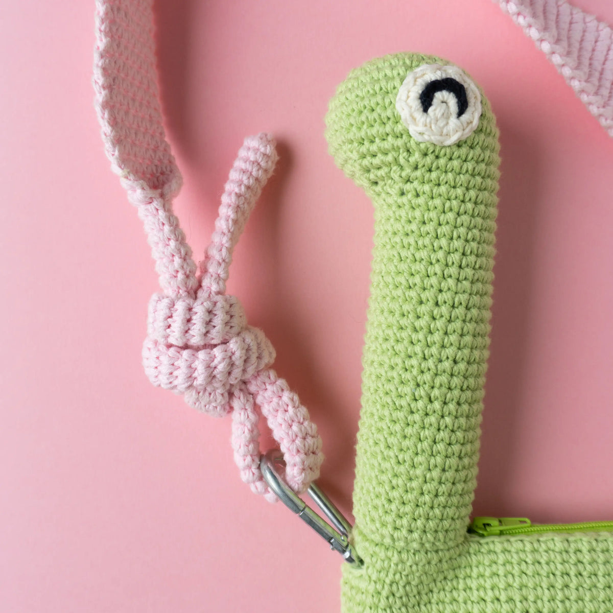 Crocheted brachiosaurus dinosaur bag on a pink background.