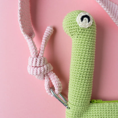 Crocheted brachiosaurus dinosaur bag on a pink background.