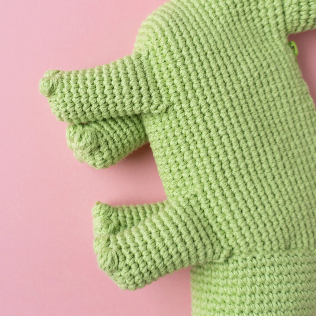 Crocheted brachiosaurus dinosaur bag on a pink background.