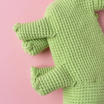 Crocheted brachiosaurus dinosaur bag on a pink background.