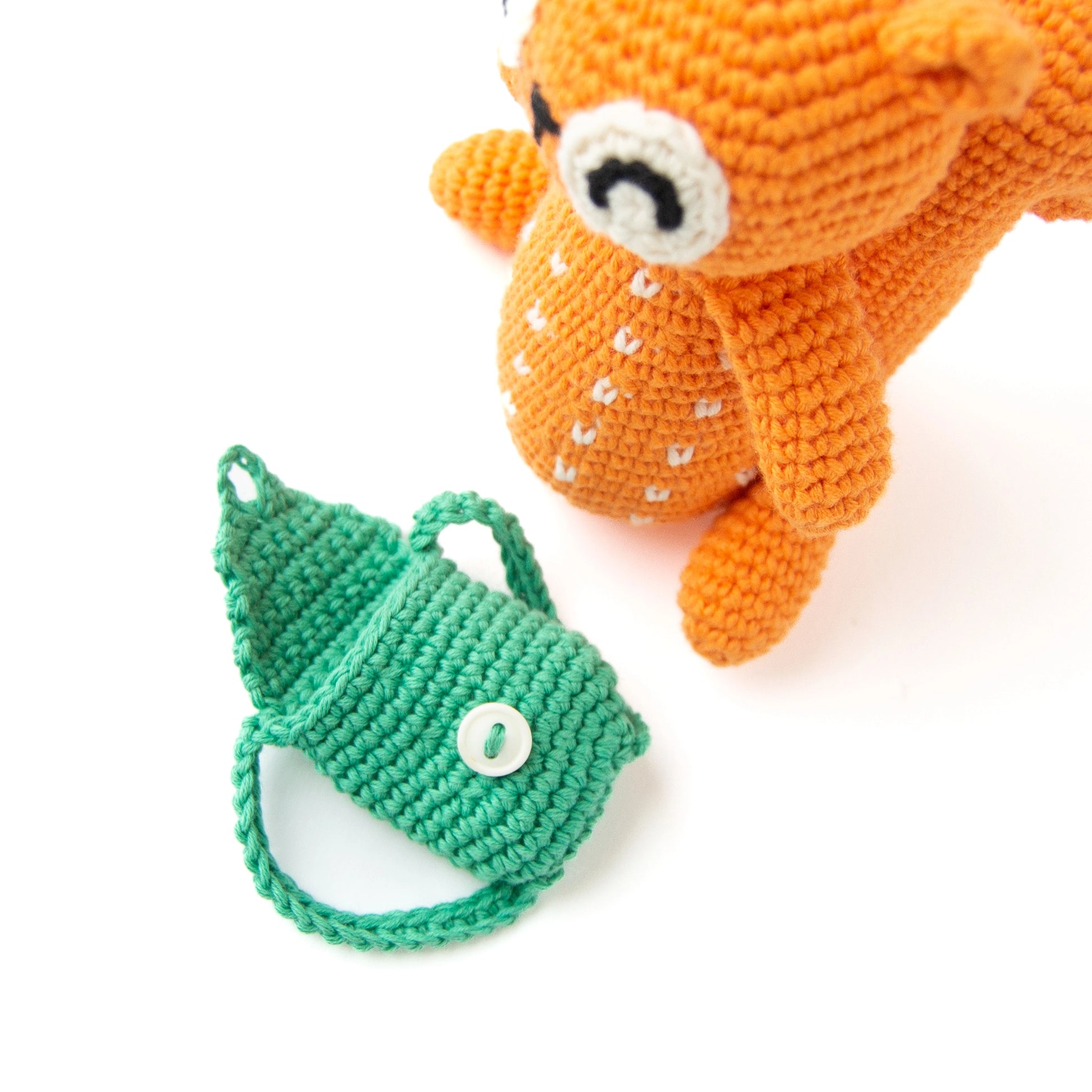 Crocheted orange squirrel with a green backpack in front of it